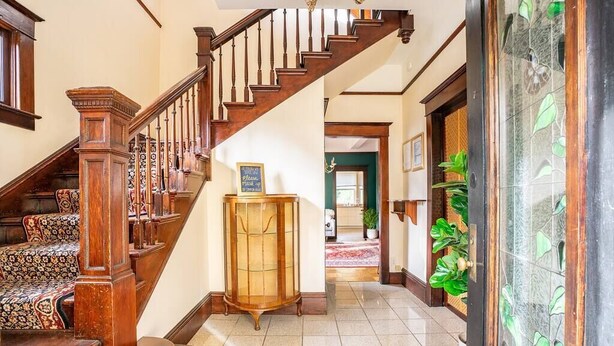 Un magnifique escalier en bois, doté de rampes et de marches recouvertes d’une moquette à motifs, mène à une pièce.