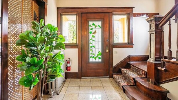 Un escalier en bois menant à une porte dotée d’un panneau de verre, un pot de fleurs et un extincteur.