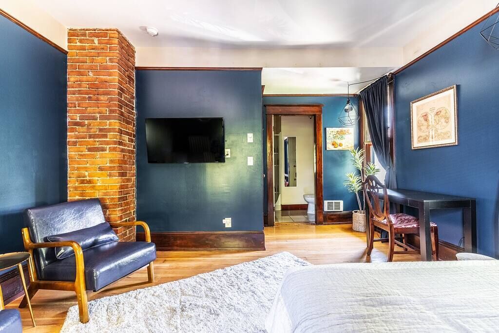 A room with a brick accent wall, a flat-screen TV, a bed, a desk, and a chair.