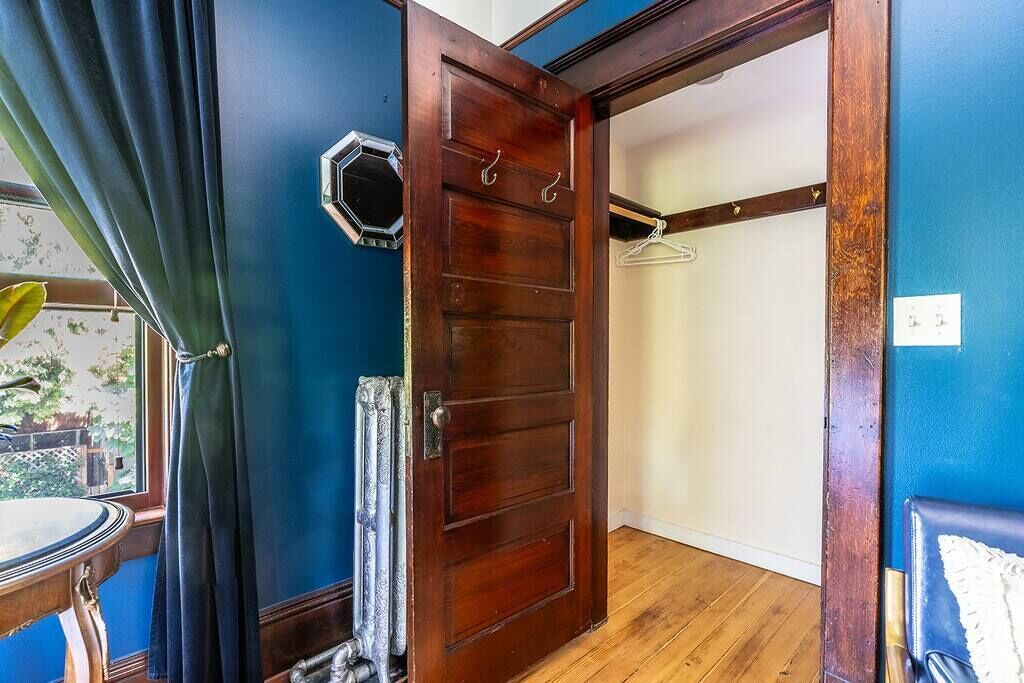 Ein Zimmer mit Holztür, Kleiderhaken und einem mit Vorhängen drapierten Fenster.