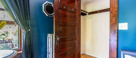 Une pièce avec une porte en bois, un porte-manteau et une fenêtre avec des rideaux.