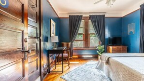 A bedroom with a bed, a desk, a chair, a television, and a window with curtains. - Charming Room in Historic BnB with Parking - Rm 5 (Seattle)