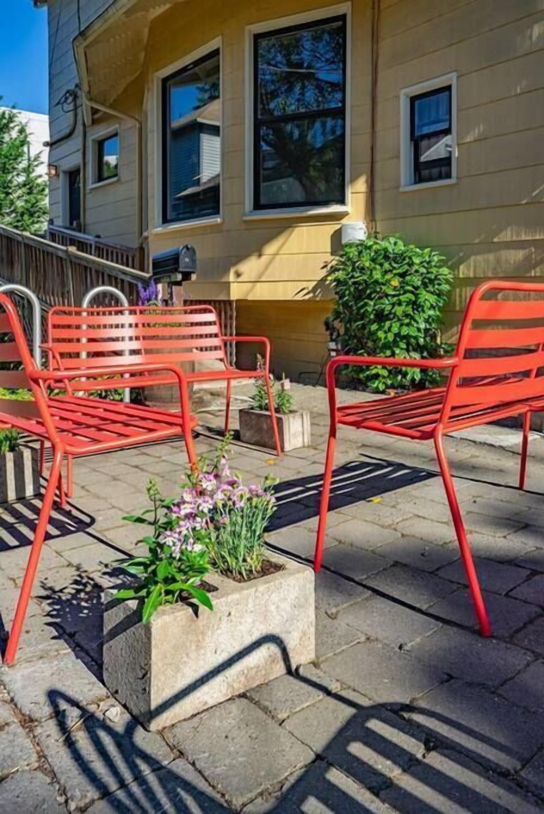 A building with a yellow facade, outdoor seating area with red metal chairs, and potted plants.
