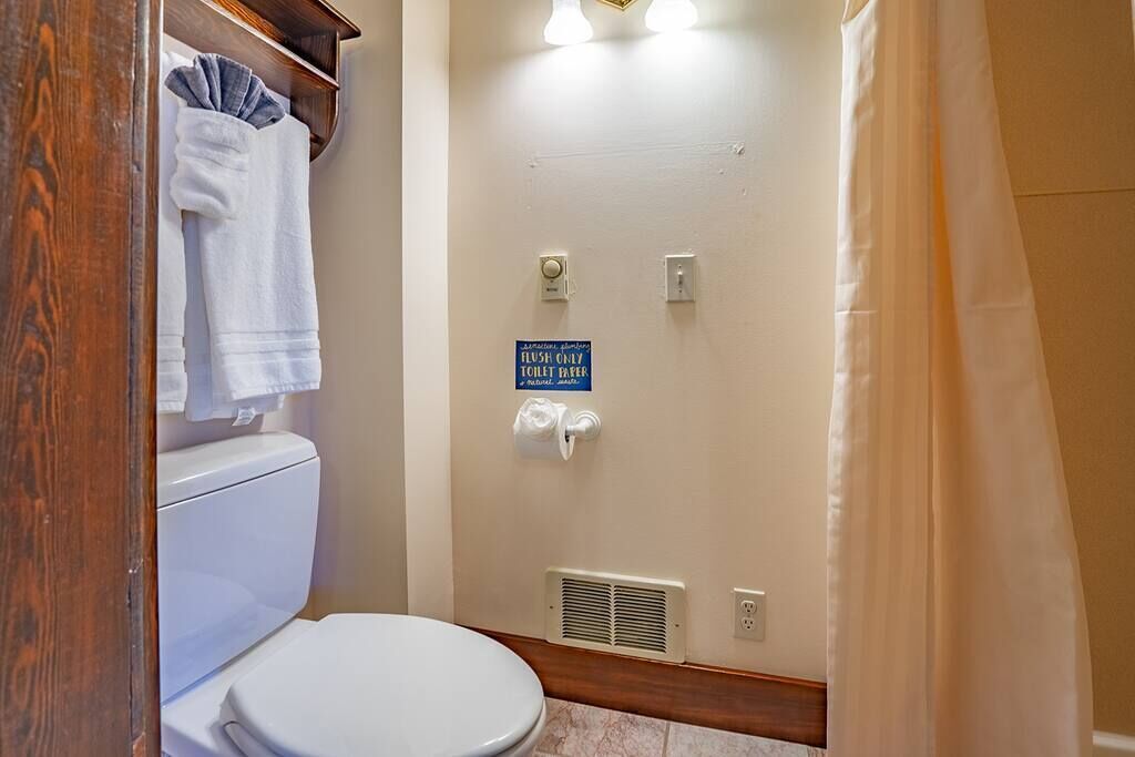 A bathroom with a toilet, a shower, and a sign indicating it is a flush-only toilet room.