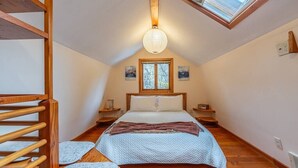A bedroom with a sloped ceiling, a skylight, a bed with a blue quilt, wooden flooring, and a wooden ladder. - Charming two-level retreat (Seattle)