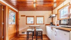 A kitchen with wooden flooring, a table with two stools, a microwave, and a refrigerator. - Charming two-level retreat (Seattle)