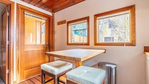 A compact kitchen with wooden cabinetry, a small table, two stools, and a trash bin. - Charming two-level retreat (Seattle)