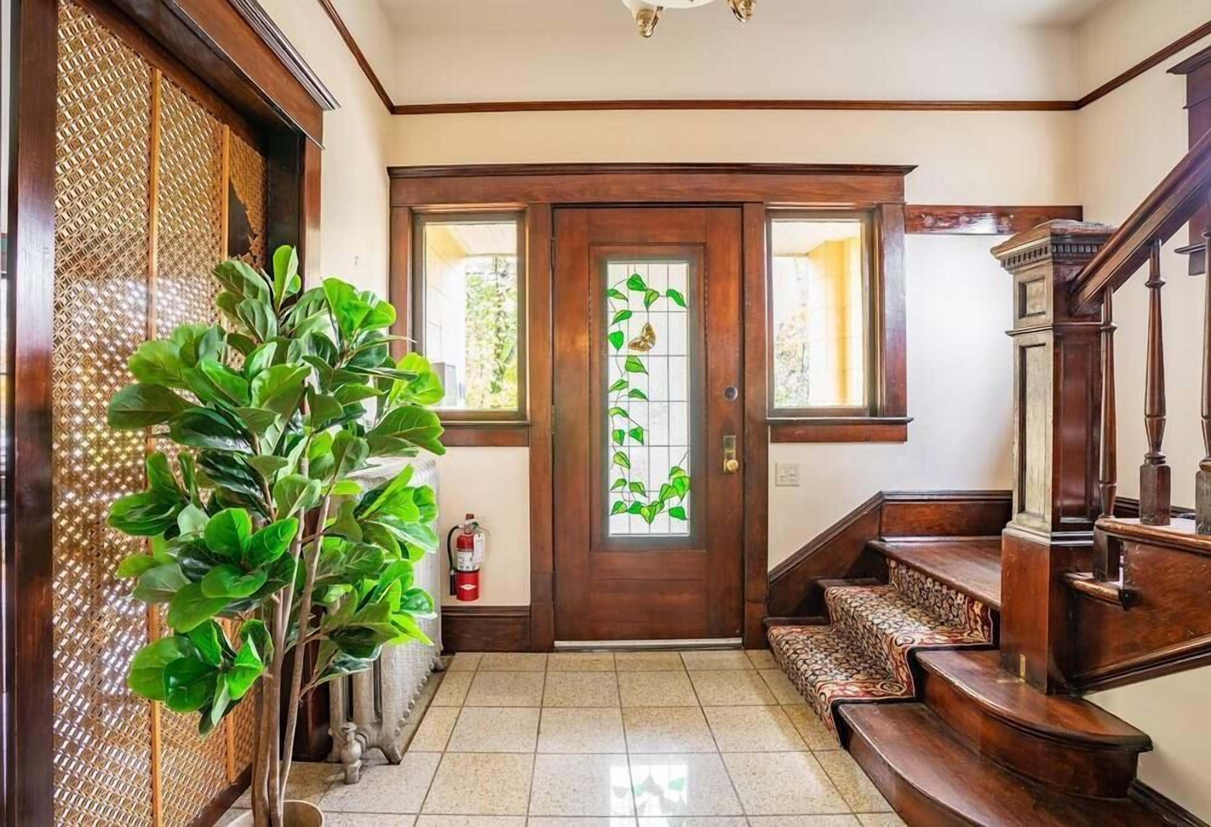 Uma escada de madeira leva a uma porta com painel de vidro, um vaso de planta e um extintor de incêndio.