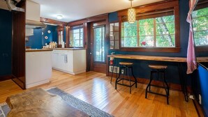 A kitchen with wooden flooring, a central island, bar stools, and a window with a view of greenery. - Charming 1bd Suite in Cap Hill - With Parking (Seattle)