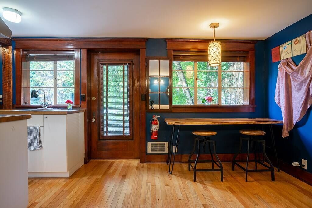 A kitchen with wooden floors, a bar area with stools, and large windows with blinds.