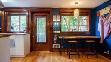 A kitchen with wooden floors, a bar area with stools, and large windows with blinds.