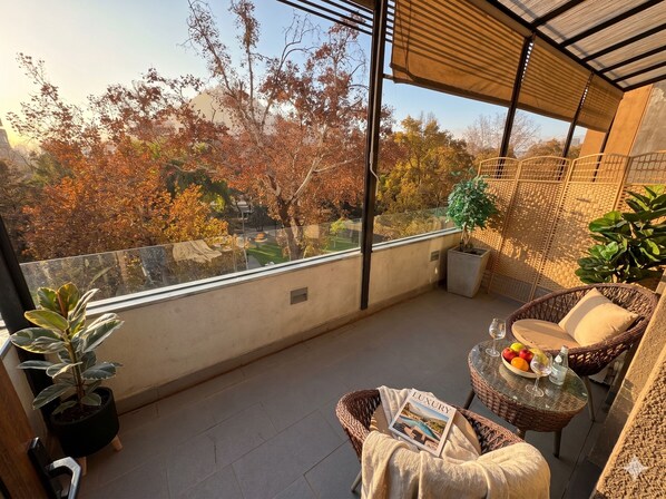 A balcony with a wicker chair, a small table with a magazine, and potted plants. - BHB Hotel Boutique (Santiago)