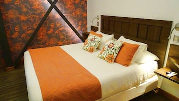 Ein ordentlich bezogenes Bett mit orangefarbener Decke und blumigen Kissen, ein Holzkopfbrett und ein Nachttisch mit Lampe.