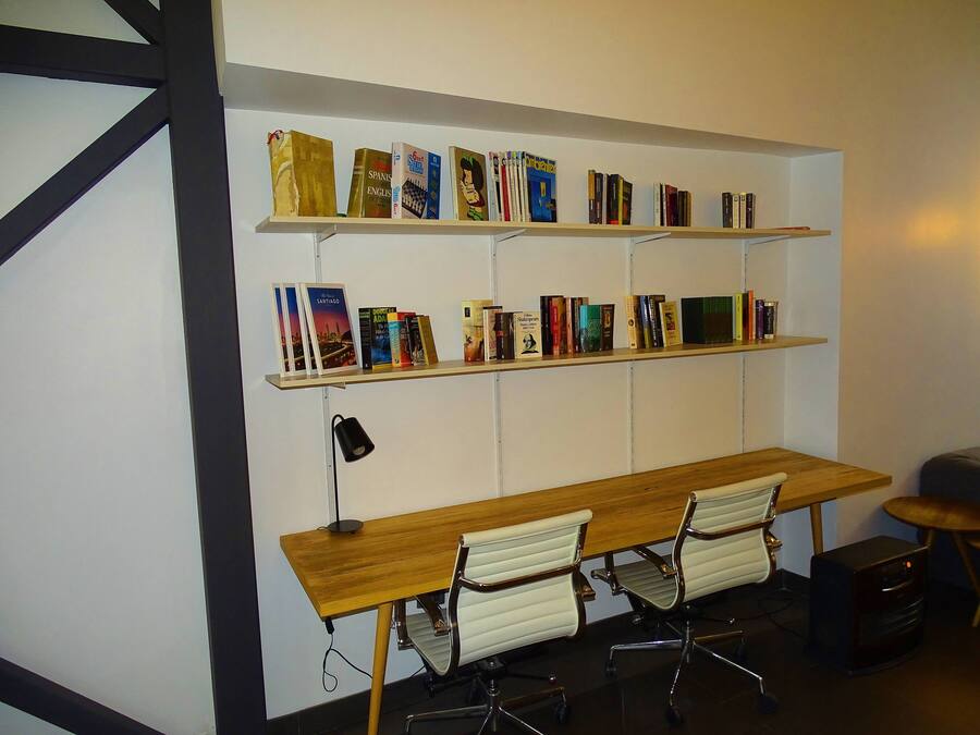 A workspace with a wooden desk, two white office chairs, and a bookshelf with various books.