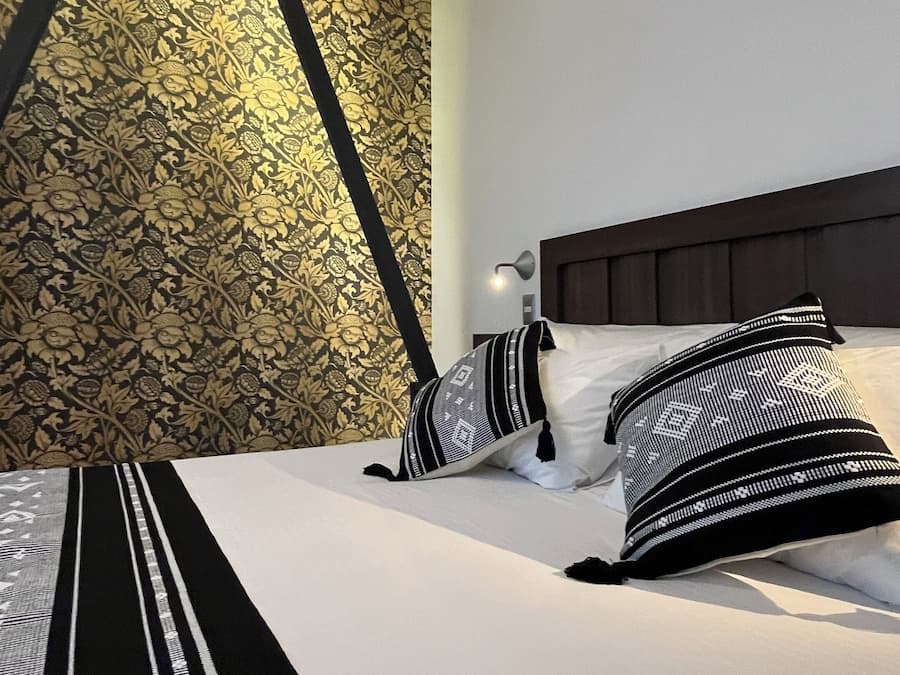 A hotel room with a bed, a nightstand, a wall with a patterned wallpaper, and a ceiling light.