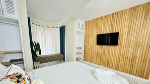 Et hotelværelse med seng, fjernsyn monteret på en trævæg, en bænk og en potteplante.