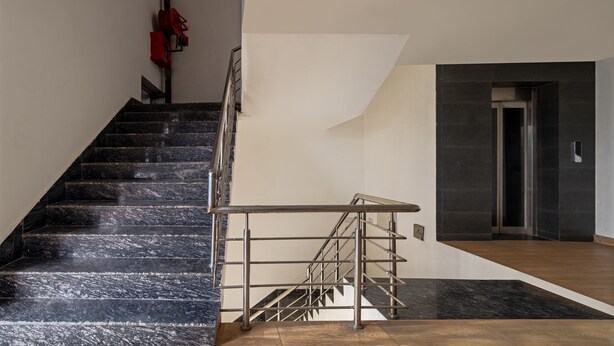Una escalera con escalones de mármol negro, barandilla de metal y un rellano de madera.