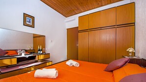A hotel room with an orange bedspread, a wooden wardrobe, a mirror, and a small table with a vase. - Studio apartment 2304/100332 (Istria - Rovinj), 2500m from the beach (Rovinj)