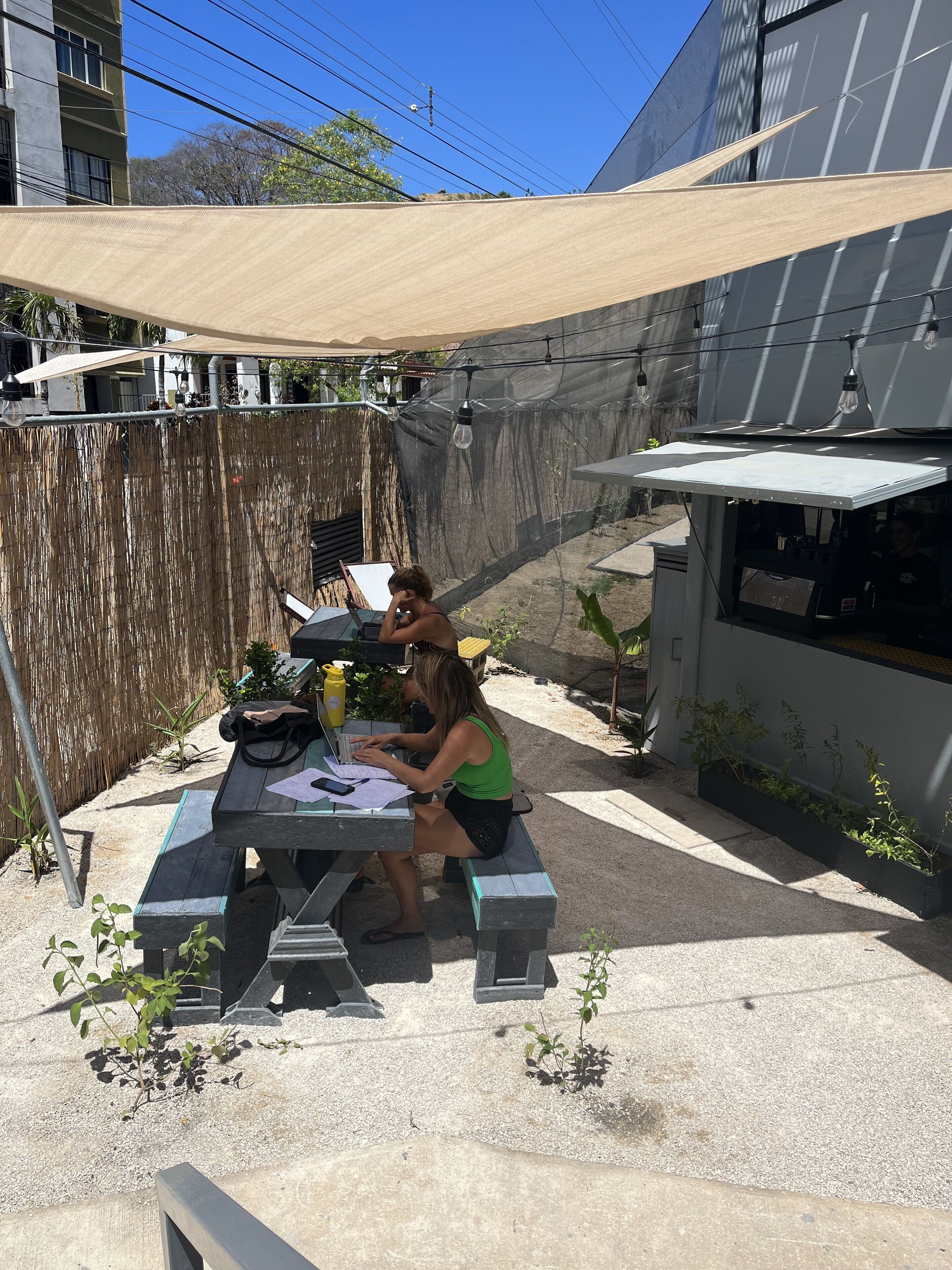 An outdoor patio with a table and chairs, a shaded area, and a building in the background.