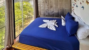 A bedroom with a large bed, a view of greenery outside, and a ceiling with a light fixture. - Pupa House  (Tamarindo)