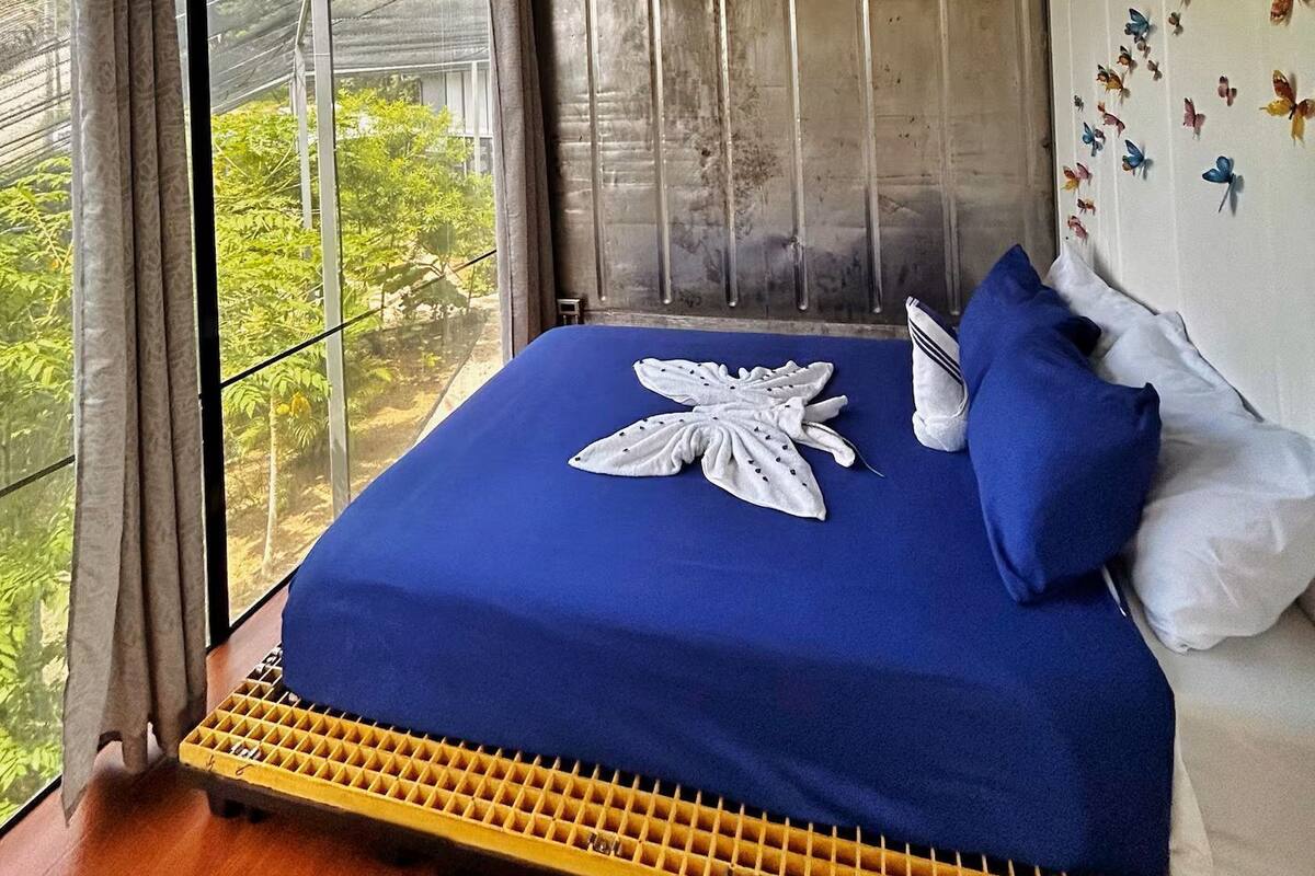 A bedroom with a large bed, a view of greenery outside, and a ceiling with a light fixture.