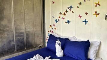 Ein Bett mit blauer Bettdecke, weißen Kissen und einem Handtuch, das zu einer Blume geformt ist.