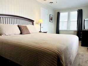 Una camera d'albergo con un letto grande, una lampada da comodino, un comò e una finestra con tende.