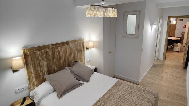 A modern bedroom with a large bed, wooden headboard, bedside lamps, and a geometric throw blanket.