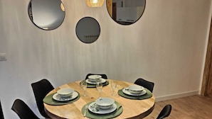 A dining area with a round wooden table set for four, surrounded by black chairs. There are three hanging spherical light fixtures above the table.