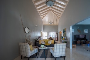 A living room with a high ceiling, a sofa, two armchairs, a coffee table, and a TV.