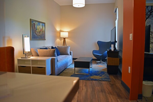 A modern living room with a sofa, a coffee table, a lamp, and a painting on the wall.