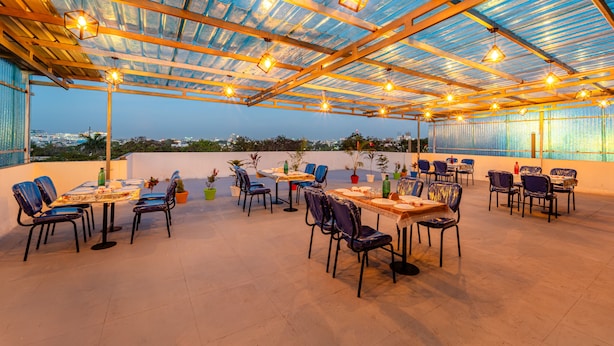 Un área de comedor al aire libre con mesas y sillas, techo de vidrio y plantas en macetas.