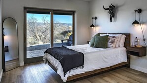 A bedroom with a large bed, a ceiling fan, a bull sculpture, and a view of the outdoors. - Peaceful creek-country escape that feels almost magical, with a private trail to Oak Creek and a cedar hot tub off the master bath. Very private, yet 10 min to wineries and 25 min to Sedona. Usually 10-15 degrees cooler than Phoenix. (Cornville)