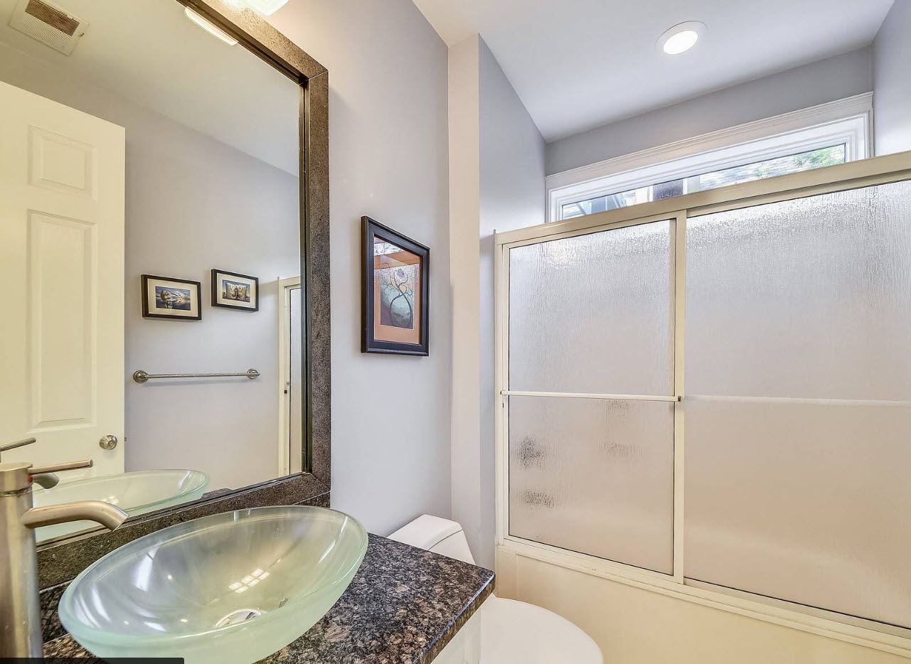 A bathroom with a glass sink, a mirror, and a frosted glass shower enclosure.