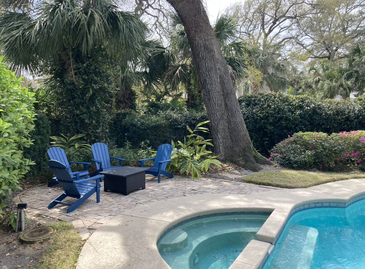 A backyard with a swimming pool, blue Adirondack chairs, and a small table.