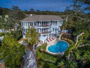 A large, two-story house with a swimming pool, surrounded by lush greenery and trees.