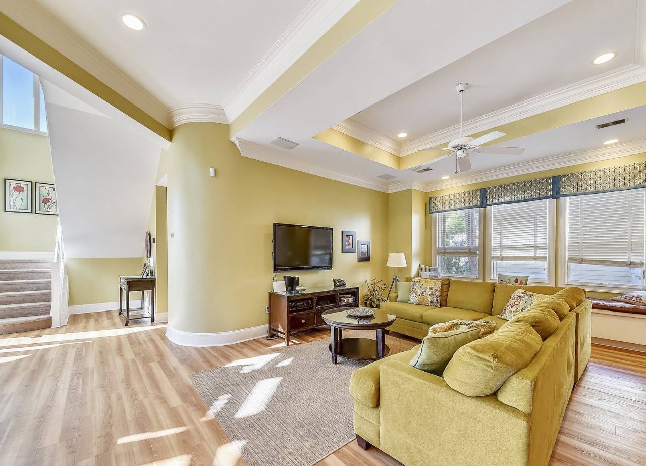 A spacious living room with a large sofa, a flat-screen TV, and a staircase leading to an upper level.