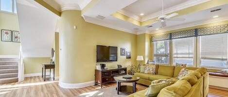 A spacious living room with a large sofa, a flat-screen TV, and a staircase leading to an upper level.
