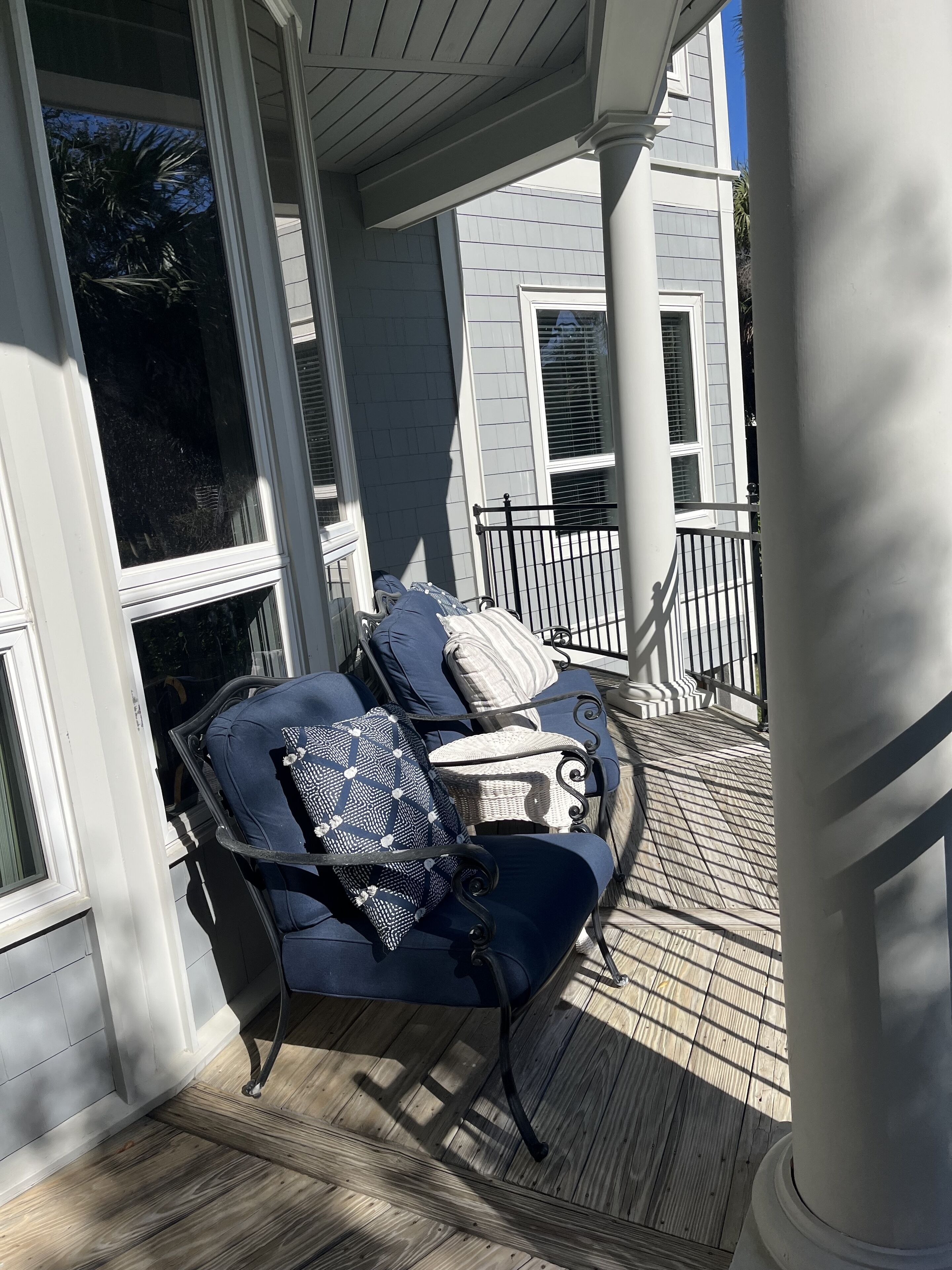A covered porch with two chairs and a table, a wooden deck, and a building with white siding and shutters in the background.