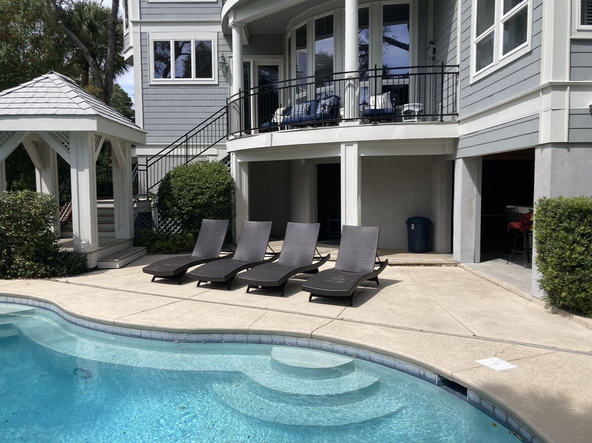 A poolside area with lounge chairs, a covered seating area, and a building with a balcony.