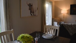 Ein Essbereich mit einem Tisch für zwei Personen, einem gerahmten Bild eines Stiers an der Wand, einer Lampe und einem Fenster mit Vorhängen.