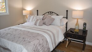 Ein ordentlich bezogenes Bett mit einem blumigen Überwurf, zwei Nachttischlampen und ein kleiner Tisch mit einer Vase und Fernbedienung.
