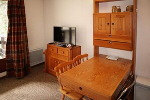 A small room with a wooden desk, a television, a cabinet, and a plaid curtain.