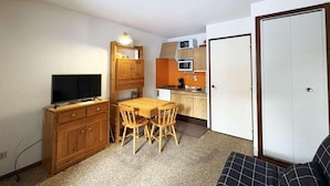 A compact living space with a kitchenette, a dining area with a table and chairs, a television on a wooden cabinet, and a door leading to another room. - 10m from ski slopes, 1st floor, balcony, ski locker, 20m², Les Orres (Les Orres)