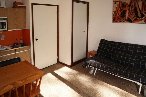 A compact living space with a kitchenette, a dining table, a sofa, and a door.
