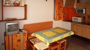 A compact room with a sofa, a small television, a table with a quilt, and a kitchenette with a microwave.