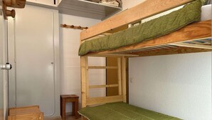 A bunk bed room with a green mattress, a wooden stool, and a small table.