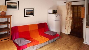 Une petite pièce agréable et chaleureuse, avec un canapé coloré, une table en bois, un réfrigérateur blanc et un four à micro-ondes posé sur le dessus.