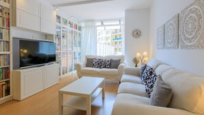 A modern living room with a flat-screen TV, white sofas, a coffee table, and bookshelves. - Apartment with private terrace, 3 bedrooms, Eixample (Barcelona)