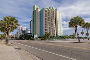 A tall, multi-story hotel with a light green and white facade, located at a street corner with palm trees and a clear sky. - Oceanfront Penthouse, Amazing Views, Walk to Conv Center, Attractions & Dining (Myrtle Beach)